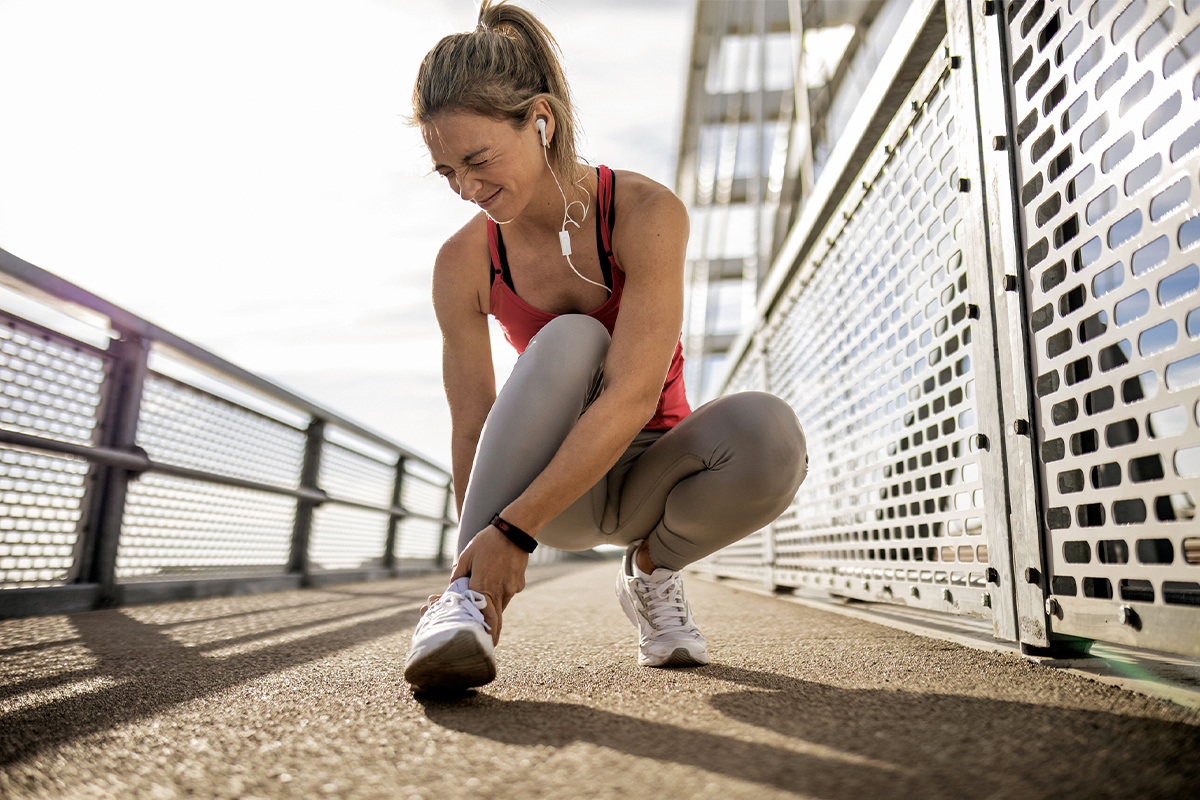 A woman outside running is hunched over in pain gripping her ankle, requiring broken ankle treatment in San Francisco.